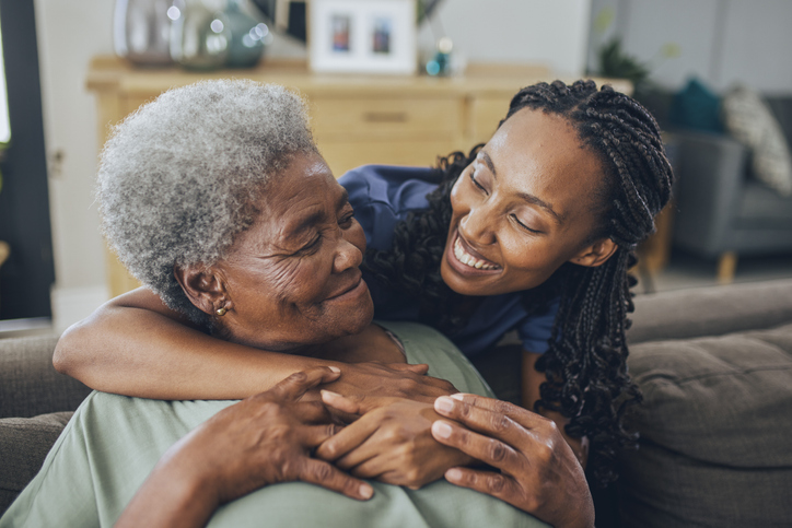 Portrait of a senior woman and a young female nurse hugging on the couch